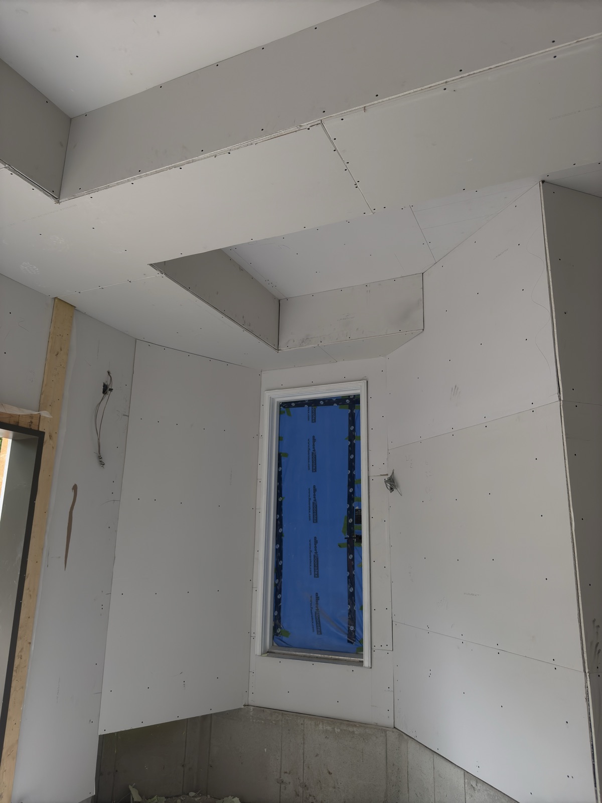 Detailed drywall installation around ceiling drops and a window