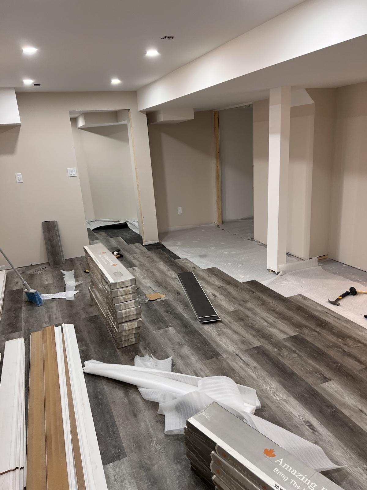 Grey luxury vinyl plank flooring installation progressing across a finished basement