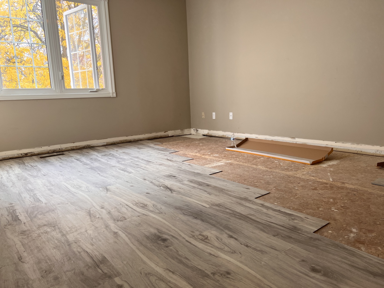 Grey luxury vinyl planks being installed across a bright room with prepared subfloor