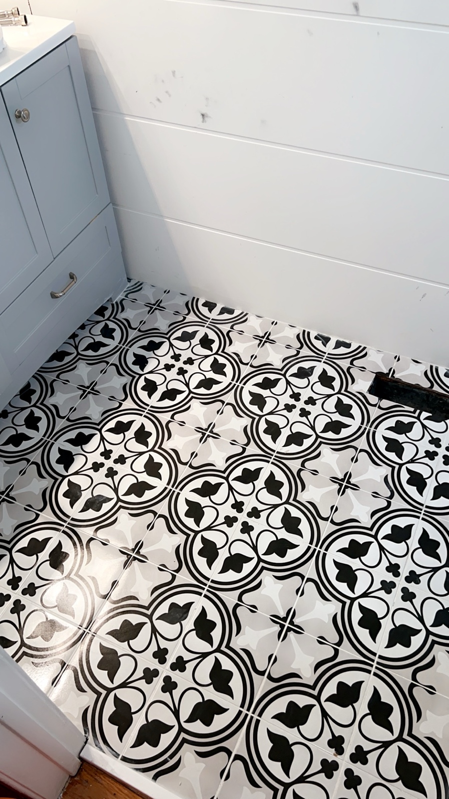 Completed black, white, and grey patterned tile floor in a compact bathroom
